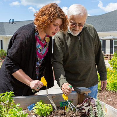 Woman assisting man to use adaptive tools to garden.